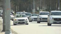 Vehicles driving through a busy British Columbia roadway with parked cars nearby.