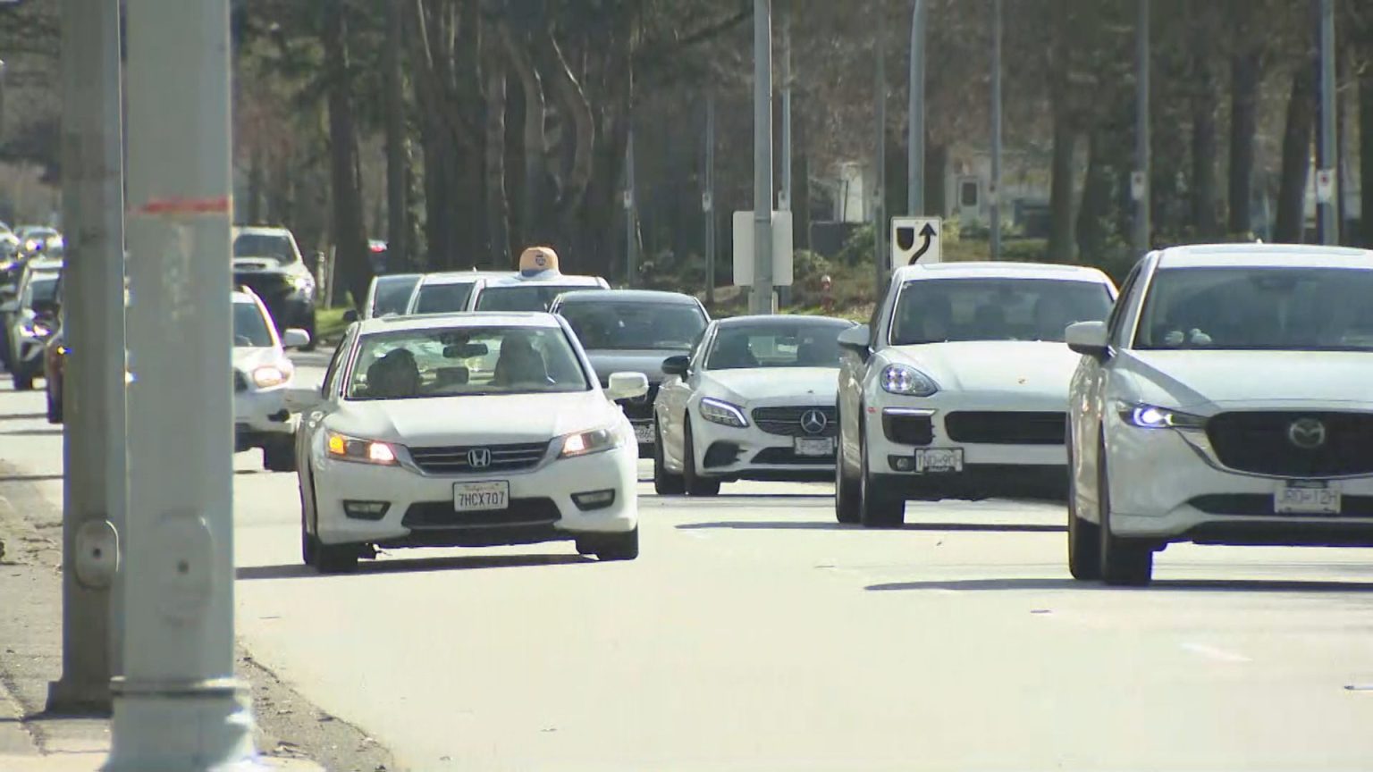 Vehicles driving through a busy British Columbia roadway with parked cars nearby.