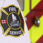 Firefighters responding to house fire in Surrey with smoke and emergency vehicles visible